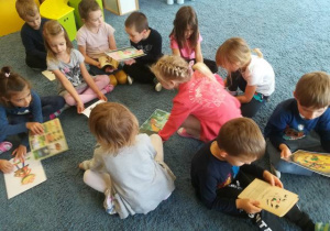 Dzieci na dywanie przeglądają ilustracje i książki o krasnalu Hałabale.